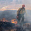A firefighter holding a driptorch walks quickly through a smoky burning field of grasses and weeds.